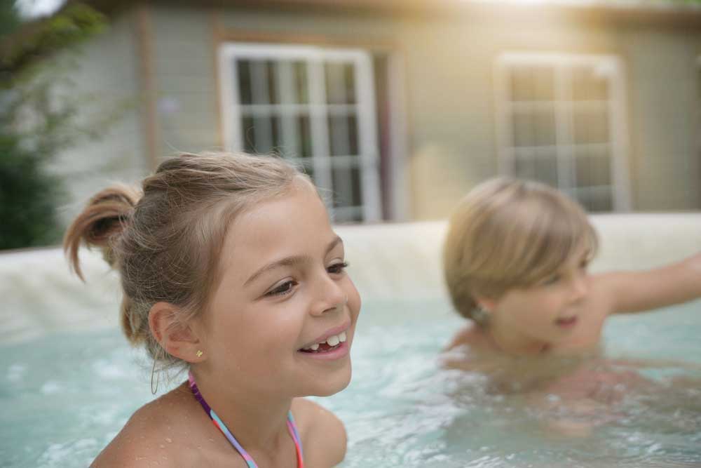 two children sat in a hot tub smiling