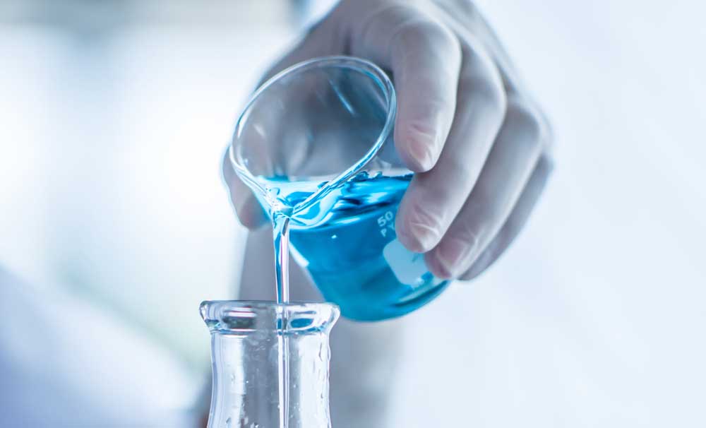 someone pouring blue liquid from one glass to another